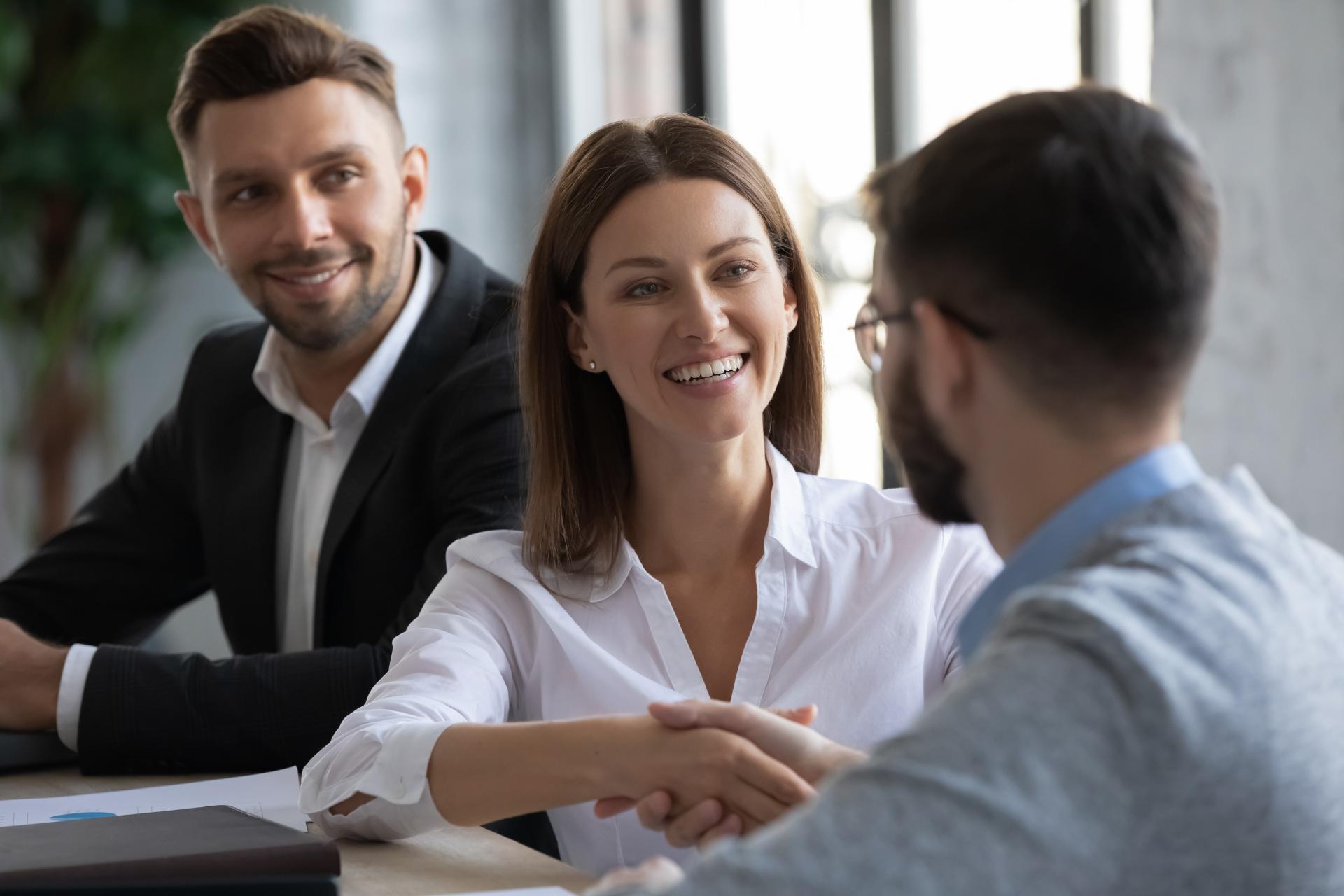 professionals shaking hands with each other with a colleague standing behind